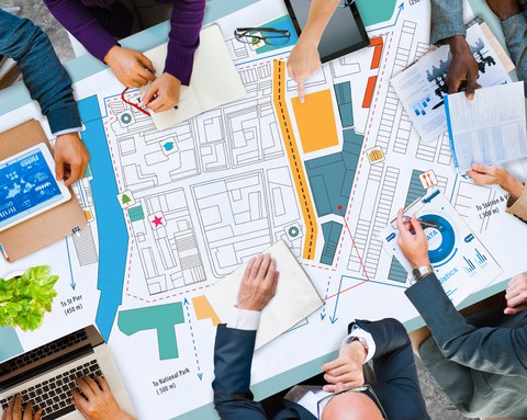 das Foto zeigt einen Tisch von oben, auf dem ein Stadtplan und Unterlagen mit daten liegen. Personen sitzen am Tisch. zu sehen sind nur deren Hände.