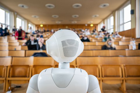 Humanoider Roboter von hinten mit Blick in den Hörsaal. 