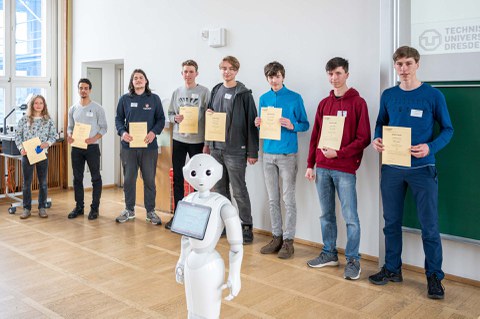 Eine Gruppe zeigt ihre Zertifikate, davor steht ein humanoider Roboter.