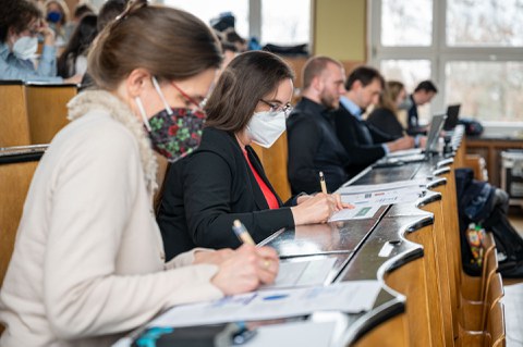 Personen sitzen im Hörsaal und machen sich Notizen.