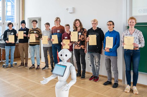 Eine Gruppe zeigt ihre Zertifikate, davor steht ein humanoider Roboter.
