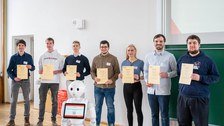 Eine Gruppe zeigt ihre Zertifikate, davor steht ein humanoider Roboter.