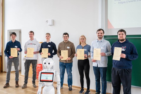 Eine Gruppe zeigt ihre Zertifikate, davor steht ein humanoider Roboter.