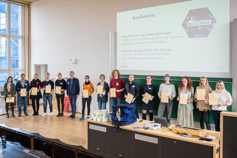 Eine große Gruppe Menschen zeigt ihre Zertifikate, im Hintergrund eine Präsentation.