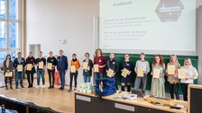 Eine große Gruppe Menschen zeigt ihre Zertifikate, im Hintergrund eine Präsentation.