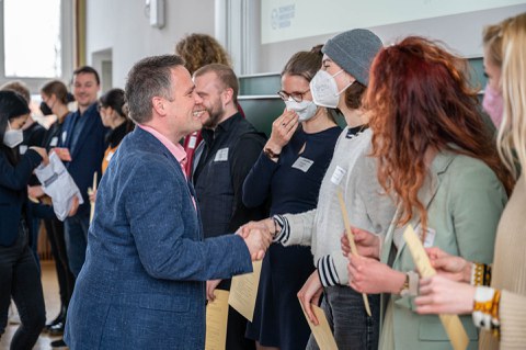 Personen bekommen ihre Zertifikate überreicht, dabei wird ihnen durch Händeschütteln gratuliert.
