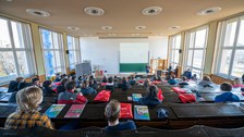 Blick in einen Hörsaal von hinten, viele Menschen, die einem Vortag folgen. 