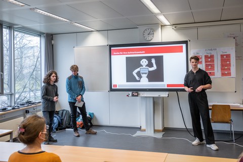 Drei Personen halten einen Vortrag mit einer Power Point Presentation. 