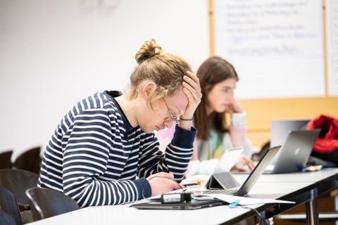 Eine Person sitzt vor einem Laptop und denkt angestrengt nach.