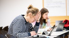 Eine Person sitzt vor einem Laptop und denkt angestrengt nach.