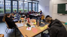 Foto von Studierenden, die in einem Seminarraum verteilt an drei Tischgruppen sitzen und an Laptops arbeiten.