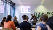 Foto vom Theorieblock Feedbackmethoden. Die Coaches sitzen in Reihen in einem Seminarraum an Tischen und schauen nach vorne auf die mit beschrifteten Zetteln beklebte Tafel.