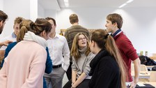 Foto von den Coaches. Sie sitzen oder stehen in einem Seminarraum und unterhalten sich.