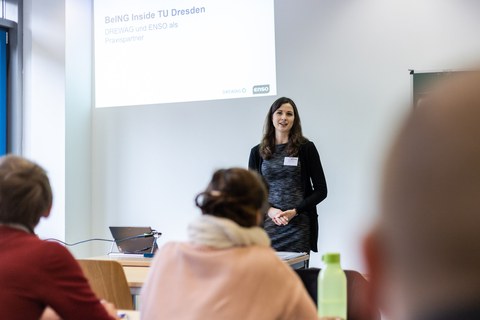 Foto von der Vorstellung der Aufgabenstellung. Eine Frau steht neben einer Tafel und erklärt etwas.