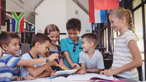 six children standing around a table and collaborating on a task; they laugh. 