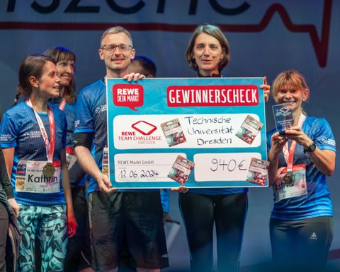 Prorektorin Universitätskultur Professorin Böhm hält den Gewinnercheck der Rewe Team Challence 2024 entgegen.