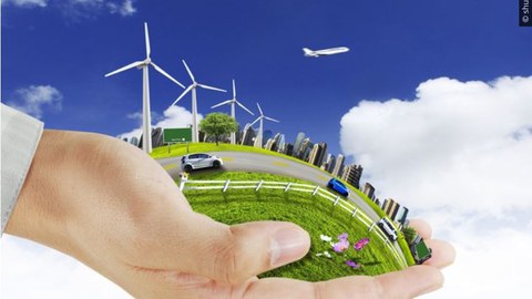 Fotomontage einer Hand die Wiesen Gebäude Straßen und Windräder schützend umfasst