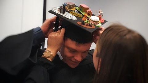 Robin Zeh, newly awarded his doctorate, receives the doctoral hat. Models related to his work are depicted on the hat.