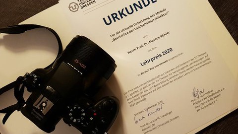 Zu sehen ist die Urkunde des Lehrpreises, daneben eine Kamera.