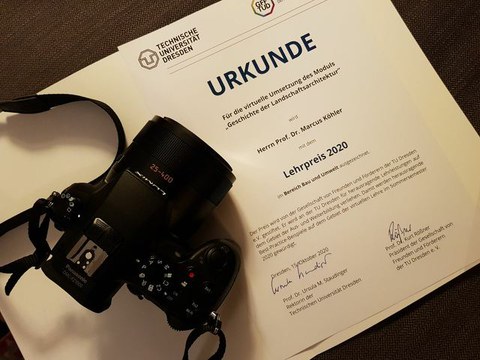 Zu sehen ist die Urkunde des Lehrpreises, daneben eine Kamera.