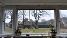 Foto zeigt den Blick aus dem Wintergarten des Wachmannshauses. Zu sehen ist eine Wiesenfläche mit angrenzenden Großgehölzen.