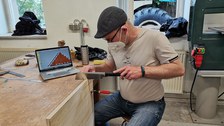 Detailfoto eines Holzelementes im Bauprozess mit Student und Werkzeug