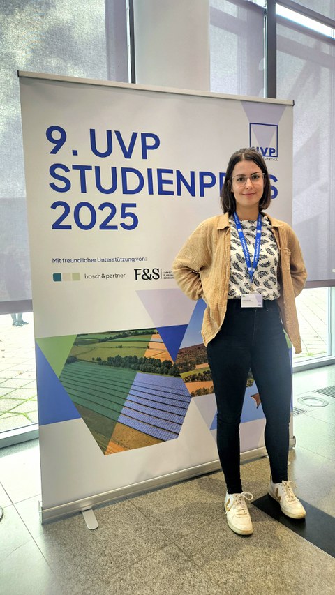 Foto von Caroline Zein vor dem Plakat zum 9. UVP Studienpreis