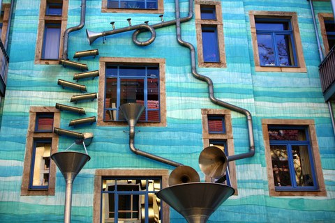 Das Foto zeigt den 'Hof der Elemente' in der Kunsthofpassage in der Dresdener Neustadt. An dem dargestellten Haus sind verschieden gebogene Rohre befestigt, durch die Regenwasser laufen kann.
