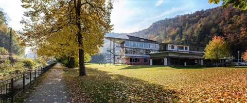 Das Foto zeigt die Rückseite des Judeich-Baus in Tharandt. Auf der großen Wiese im Vordergrund liegt Laub. Am linken Bildrand verläuft ein Bach.