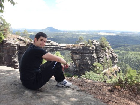 Ein Student sitzt in der sächsischen Schweiz auf einer Anhöhe und blickt lächelnd in die Kamera.
