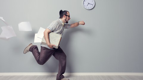 Mann rennt mit Zetteln unterm Arm mit Blick auf die Uhr