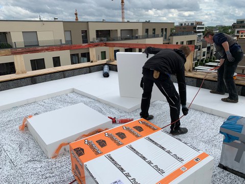 Zwei Handwerker verlegen Dämmplatten auf einem Flachdach.