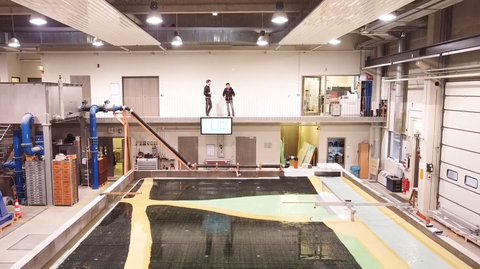 Physikalischer Modellversuch zum Retentionsraum Oberfüllbruch im Hubert-Engels-Labor, auch genannt Wasserbauhalle. Vorne ist das Modell zu sehen mit Wasser befüllt und im Hintergrund diskutieren zwei Menschen über das Experiment.
