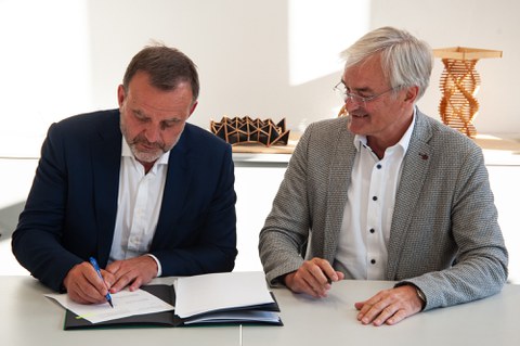 Die beiden Direktoren sitzen gemeinsam am Tisch und unterzeichnen einen Vertrag