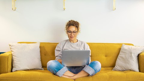 Frau sitzt mit Laptop auf dem Sofa