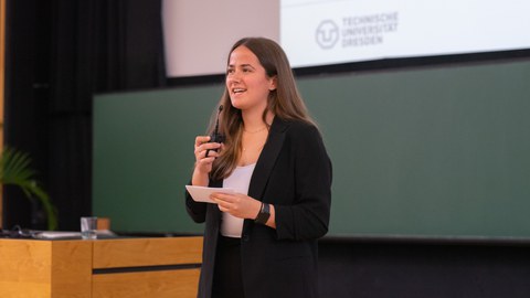 Rednerin steht auf der Bühne und spricht ins Mikrofon