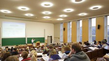 Foto von einem Seminarraum. Der Dozent spricht und es sind viele Studierende anwesend.