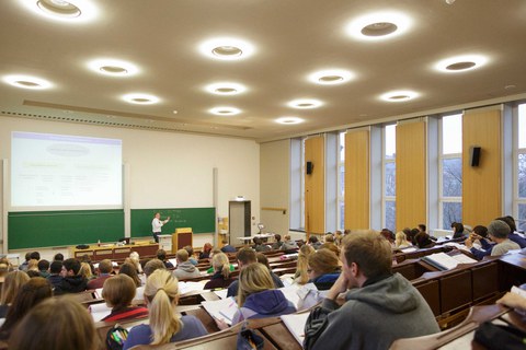 Foto von einem Seminarraum. Der Dozent spricht und es sind viele Studierende anwesend.