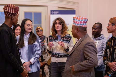 An international group listens to a young woman holding a note in her hand.