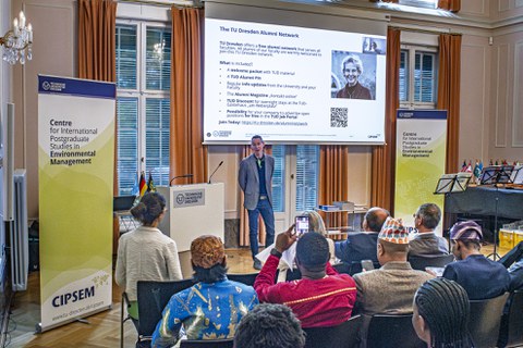 Jeremiah Peterson speaks to the participants of the event, with the audience in the foreground and a presentation in the background.