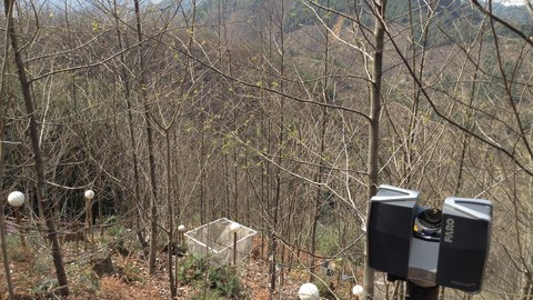 A laser scanner is on an examination area in China. The area is located on the slope and has trees. There are white balls between the trees to mark the area.