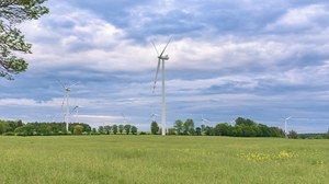 Foto zeigt eine grüne Landschaft unter blauem Himmel in der mehrere Windräder stehen.