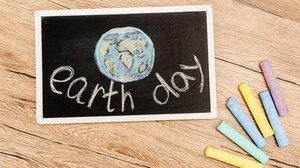 Eine Tafel mit der Erde und den Worten "earth day" drauf und farbige Kreide daneben.
