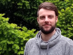 Portraitfoto eines Mannes vor einem grünem Busch