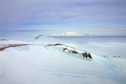 Blick über die durchs Eis stoßenden Felsen auf der Westseite der Bear Peninsula nach Süden zum ungefähr 70 bis 80 Kilometer entfernten Massiv des Mt. Murphy