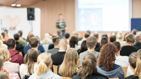 The photo shows a full lecture hall during a lecture.