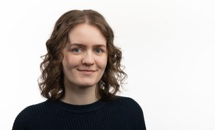 Bild von weiblich gelesener Person in schwarzen Oberteil vor weißem Hintergrund