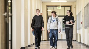 Drei Studierende gehen im Gespräch durch einen Flur des Gerhart-Potthoff-Baus; eine Person hält Unterlagen in den Händen.