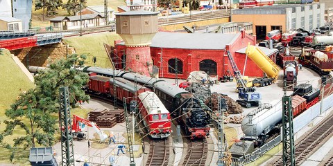 Zwei Modelleisenbahnen stehen in einem Modellbahnhof, der von Baustellen umgeben ist.
