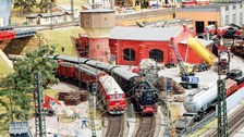 Zwei Modelleisenbahnen stehen in einem Modellbahnhof, der von Baustellen umgeben ist.